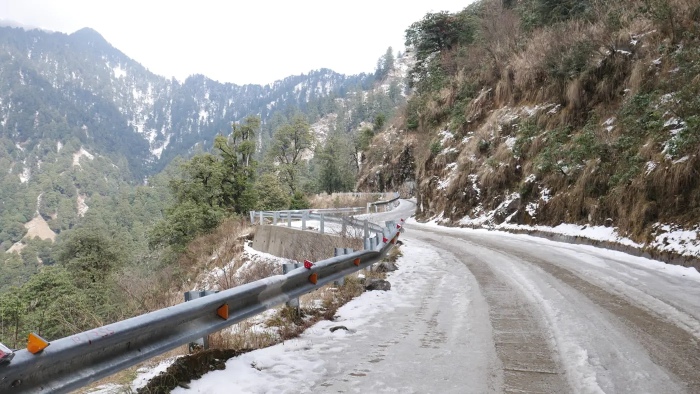 A snow-lined mountain road curving away between forested Himalayan slopes