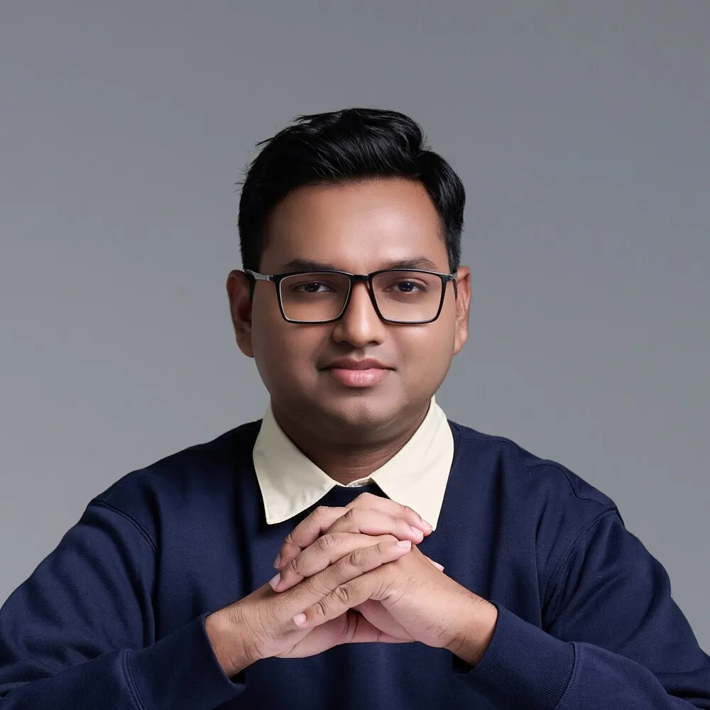 Joshua Poddoku in a navy sweater and glasses, hands clasped, looking at the camera