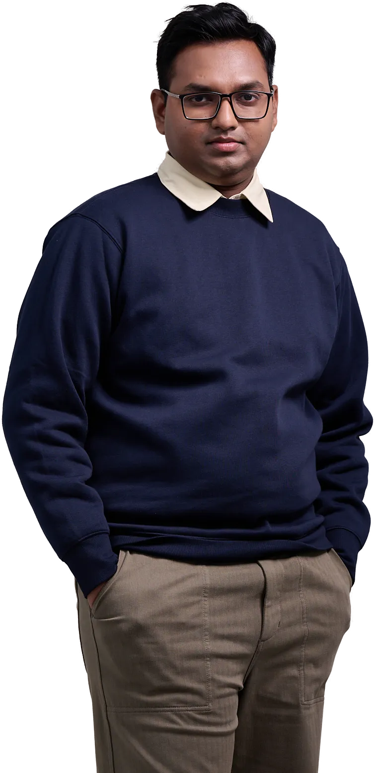 Joshua Poddoku standing in a navy sweater and glasses, hands in his pockets