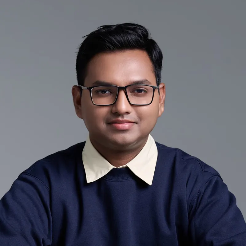 Joshua Poddoku, seated at a desk in a navy sweater and glasses