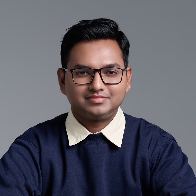 Joshua Poddoku in a navy sweater and glasses, against a blue-grey backdrop